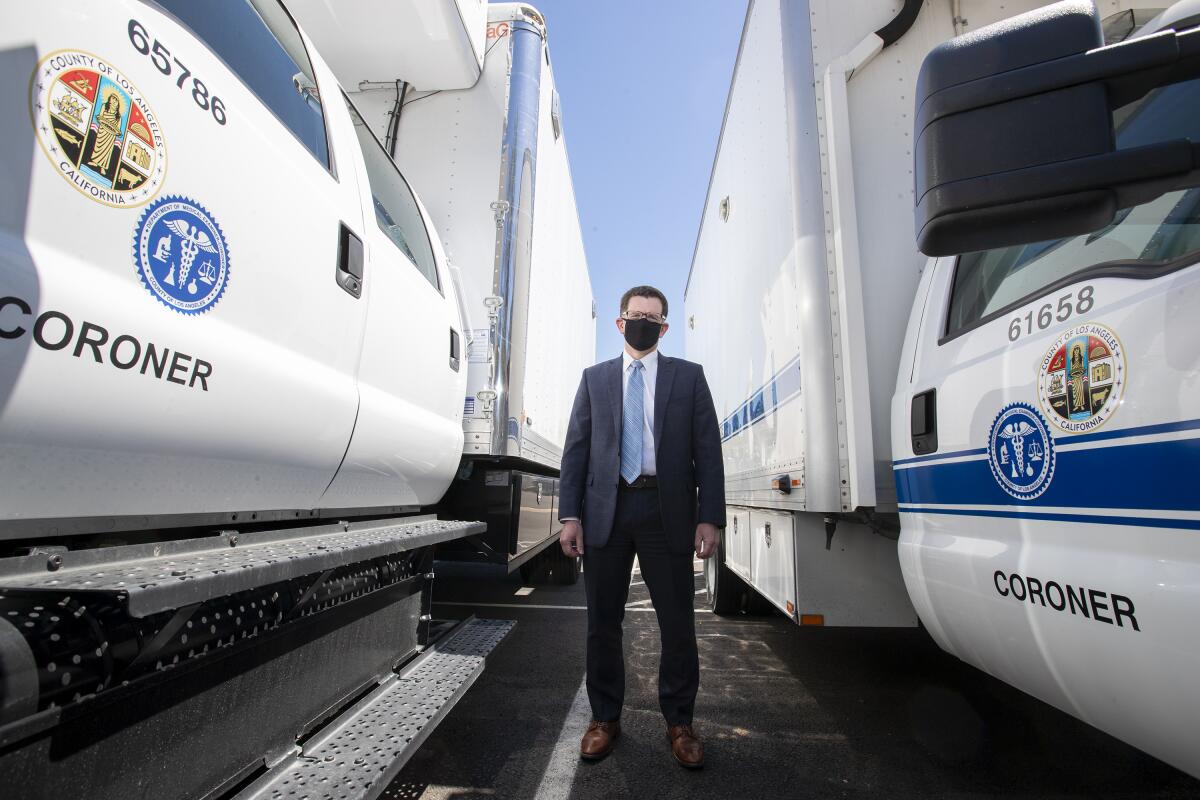 Los Angeles County Chief Medical Examiner Jonathan Lucas stands between large refrigerated trucks used to transport the dead. The coroner's office has tripled its storage space to 1,500 to be ready for a possible COVID-19 surge.