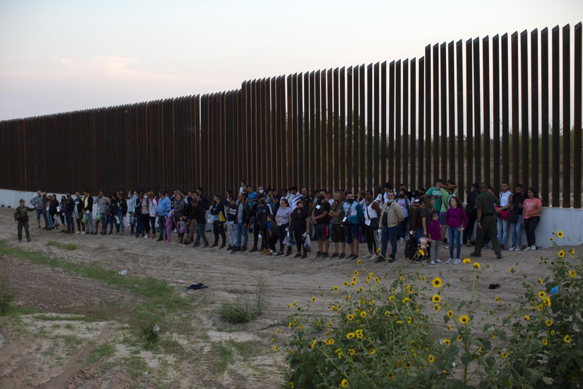 Un grupo de migrantes junto a un tramo del muro fronterizo mientras esperan a ser recogidos por la Patrulla Fronteriza