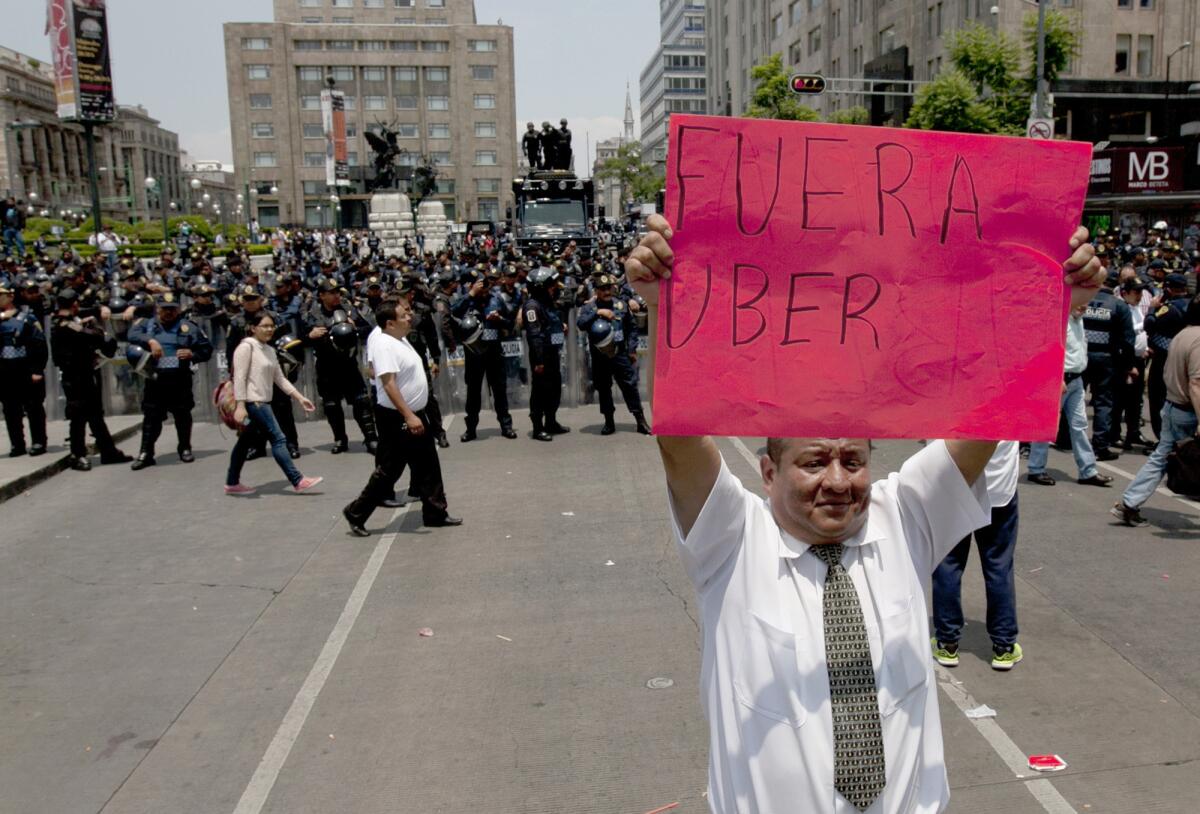En esta foto del lunes 25 de mayo de 2015, un hombrre alza el cartel de "fuera uber" frente a la policía antimotines durante una marcha por una avenida principal de la ciudad de México. Los taxistas exigen a las autoridades que arresten a los conductores de Uber e incauten sus autos. Pero Uberr sigue creciendo debido en parte al pésimo servicio que brindan los taxis tradicionales.