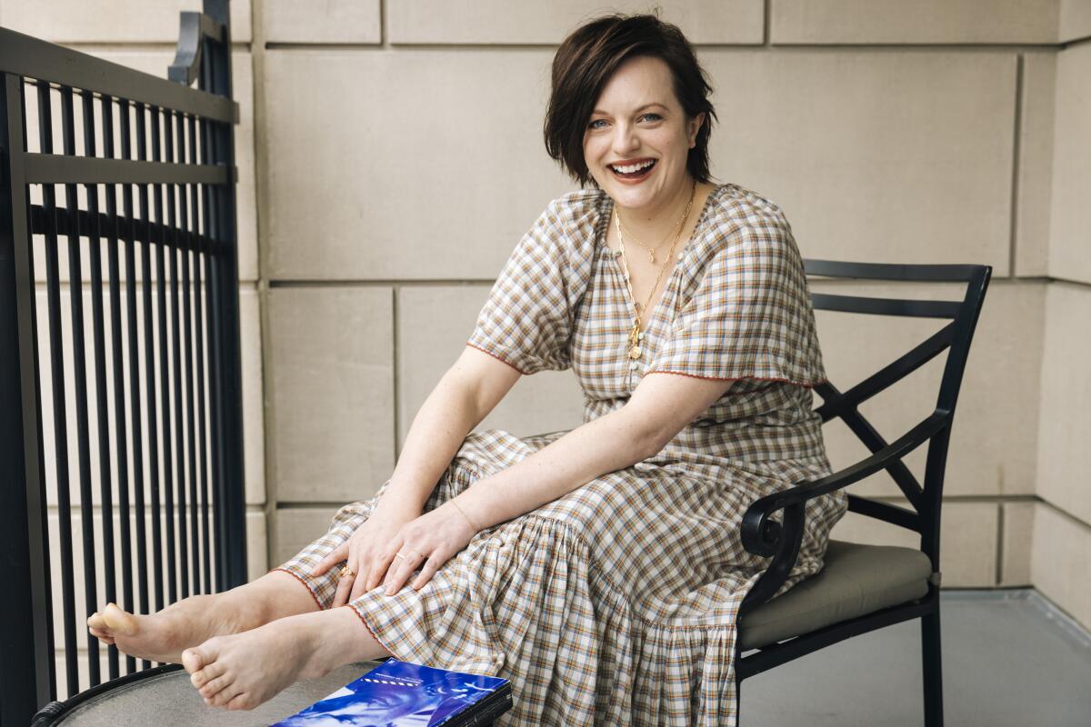 Actress Elisabeth Moss of "The Handmaid's Tale" in a brown gingham dress, seated and smiling.