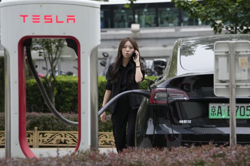 A worker stands next to a Tesla being charged in Beijing, Tuesday, May 30, 2023. China’s foreign minister met Tesla Ltd. CEO Elon Musk on Tuesday and said strained U.S.-Chinese relations require “mutual respect,” while delivering a message of reassurance that foreign companies are welcome. (AP Photo/Ng Han Guan)