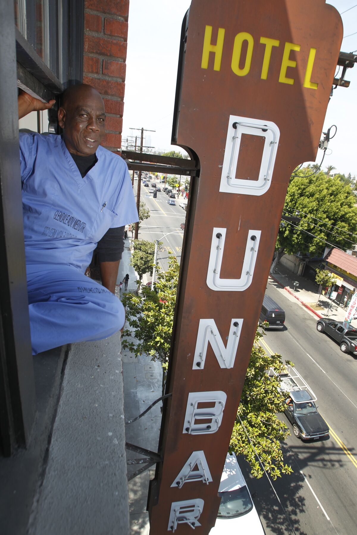 A man sits in his 5th-floor apartment window overlooking the historic Dunbar Hotel sign