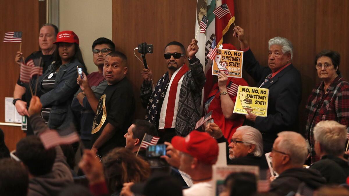 Opponents of California’s Senate Bill 54 hold signs while lining up to speak during Tuesday night’s Costa Mesa City Council meeting on whether the city should take an official stand against the “sanctuary state” law.