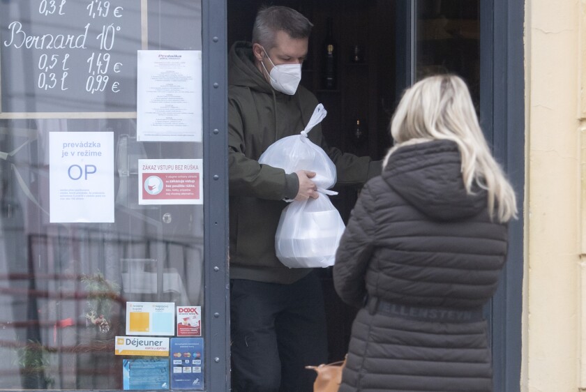 FILE- A man wearing a face mask carries a takeaway lunch from a restaurant in the Old town of Bratislava Slovakia, Nov. 25, 2021. On Monday Jan. 10, 2022, Slovakia has been easing coronavirus restrictions after a decline in new infections while the fast-spreading omicron variant is yet to fully hit the country. (Martin Baumann/TASR via AP, File)
