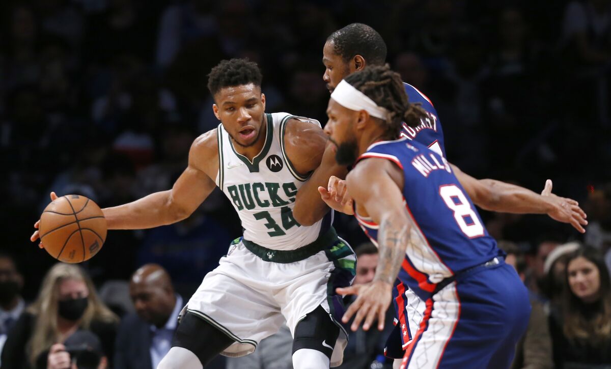 Milwaukee Bucks forward Giannis Antetokounmpo (34) is defended by Brooklyn Nets' Kevin Durant and Patty Mills (8) during the second half of an NBA basketball game Thursday, March 31, 2022, in New York. The Bucks won 120-119 in overtime. (AP Photo/Noah K. Murray)