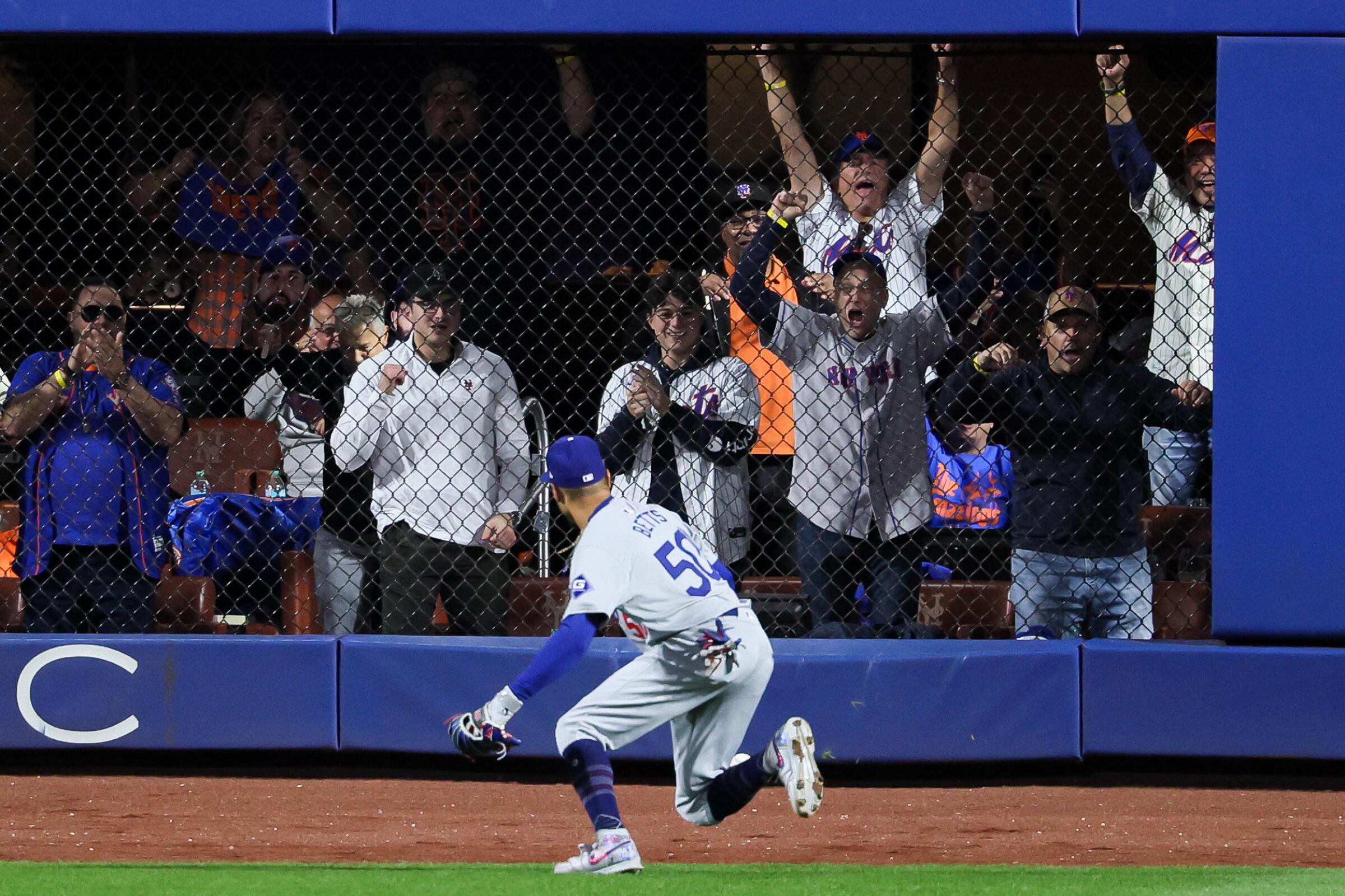 Mets fans beyond wall cheer as Dodgers right fielder Mookie Betts tries to track down a ball.