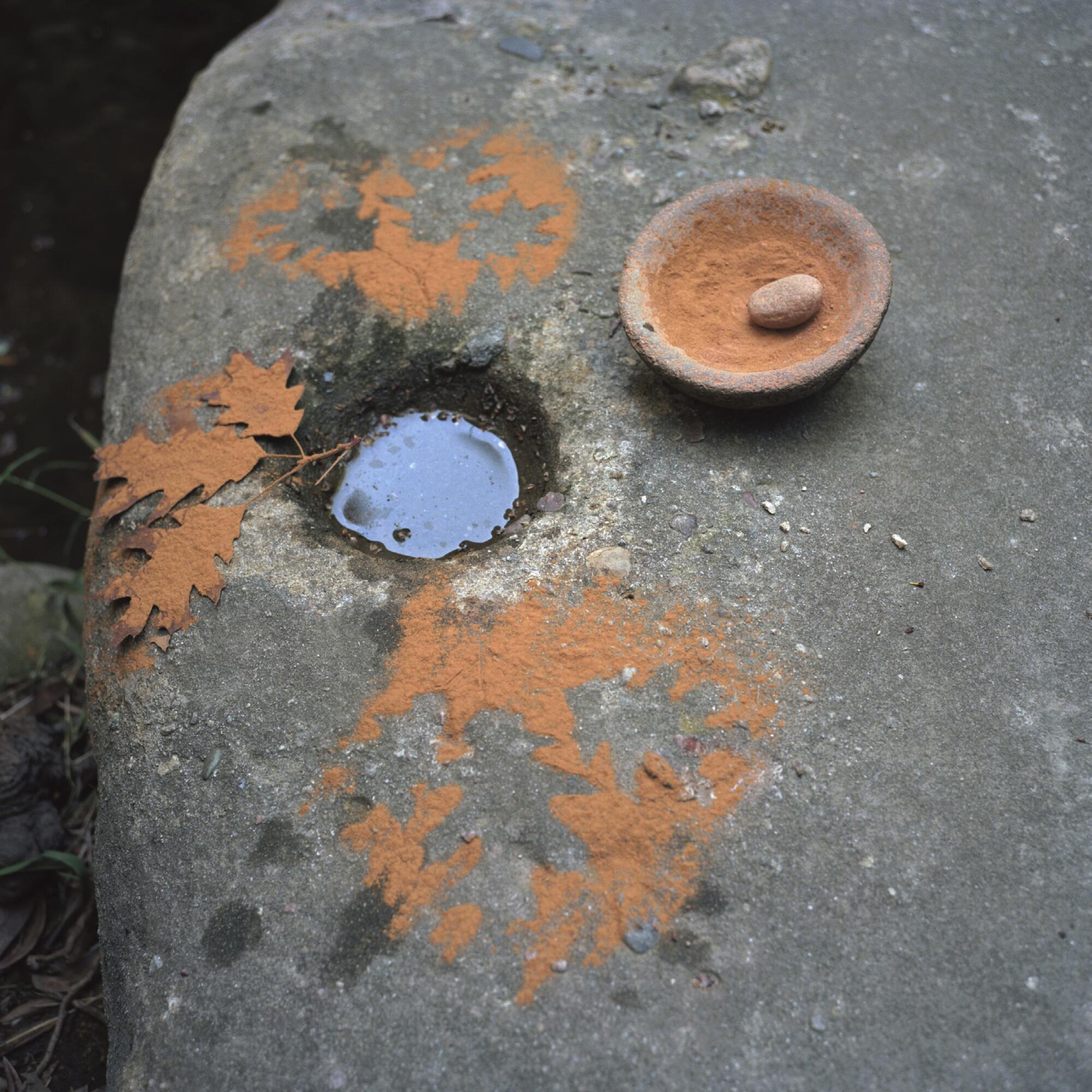 A color photograph shows a granite boulder, its mortar filled with water and framed by oak leaves and ochre pigment.