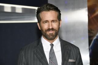 Actor Ryan Reynolds with facial hair in a black striped suit and a silver tie