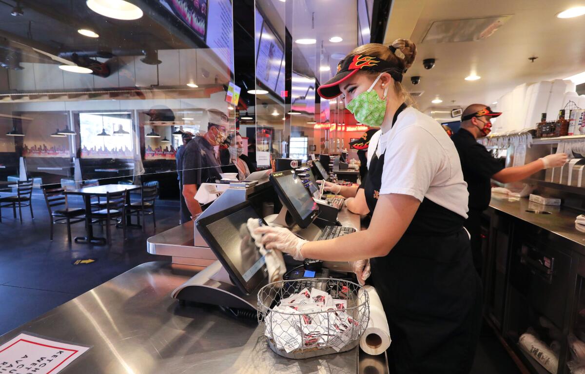 Chloe Lopez, a Phil's BBQ employee at the Rancho Bernardo location, cleans a monitor as the restaurant serves take-out customers separated by large, clear plastic panels.