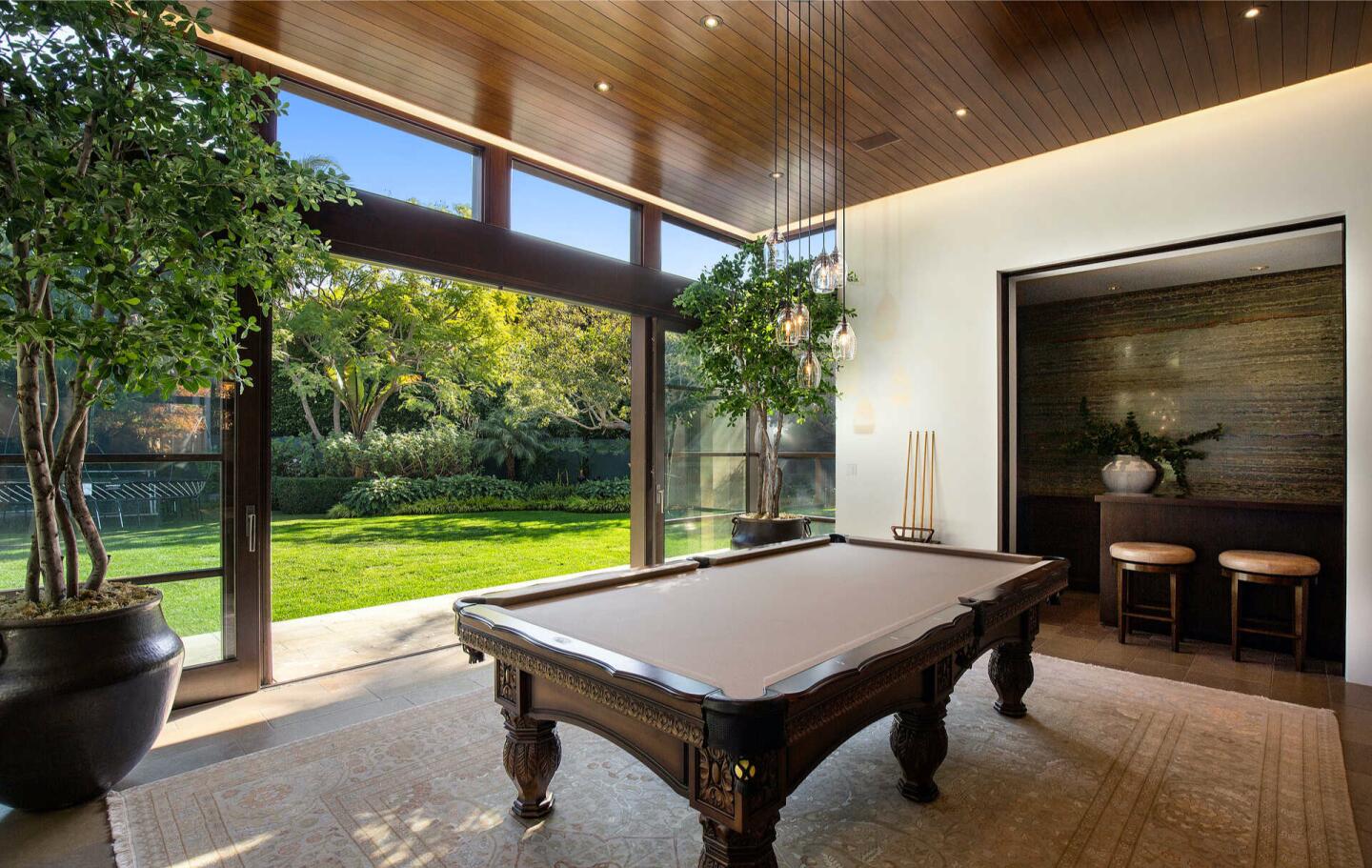 The billiards room with a pool table and glass wall overlooking trees and lawn.