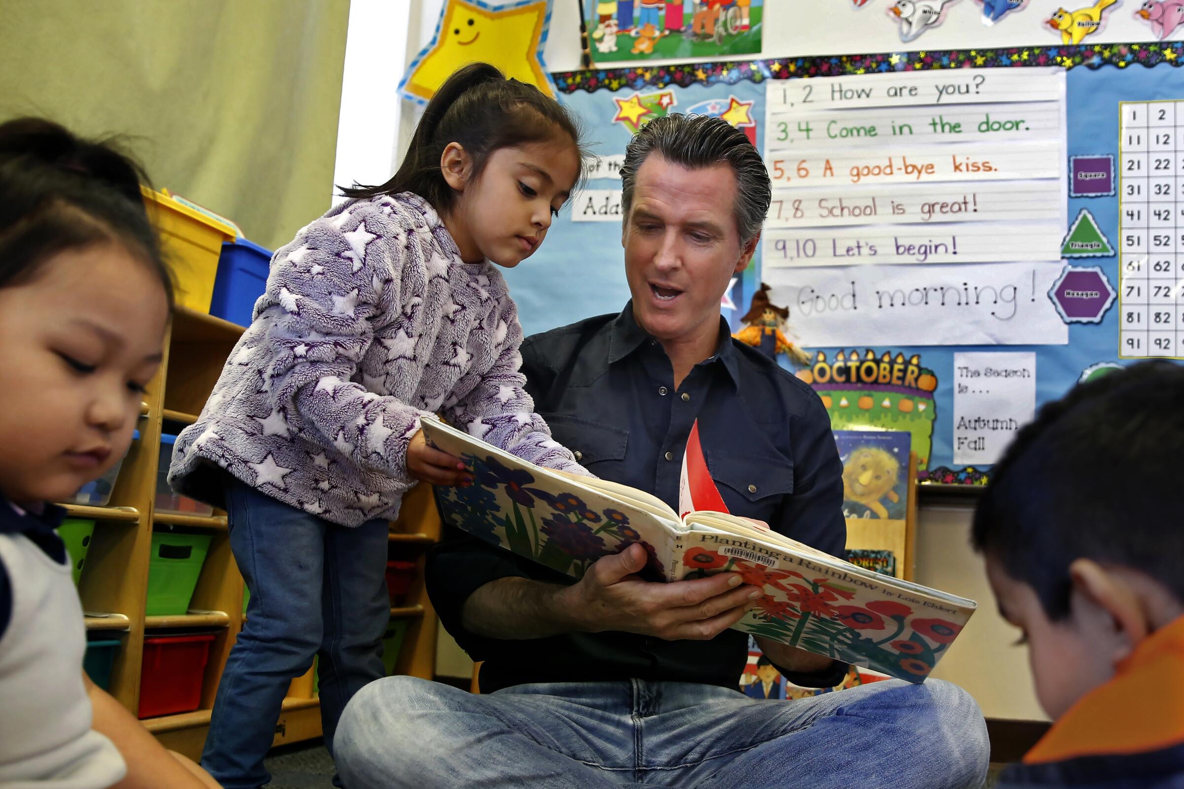 Gov. Gavin Newsom and kindergartner Priscilla Ramirez look over the book Planting a Rainbow, 