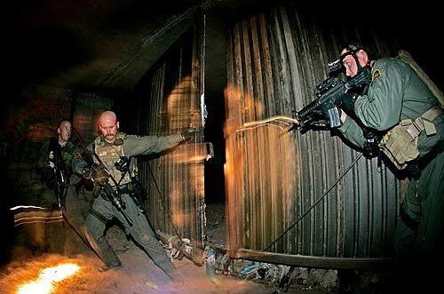 Searching for smugglers a mile inside a drainage tunnel, Border Patrol agent Jim Amstedz yanks open a steel gate that defines the U.S./Mex. border. Scott Connors,(L) and Scott Wencel hold weapons at the ready.