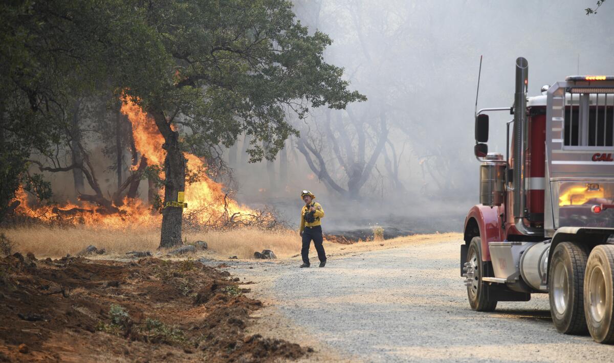 A firefighter walks near flames burning next to a road where a large truck is parked