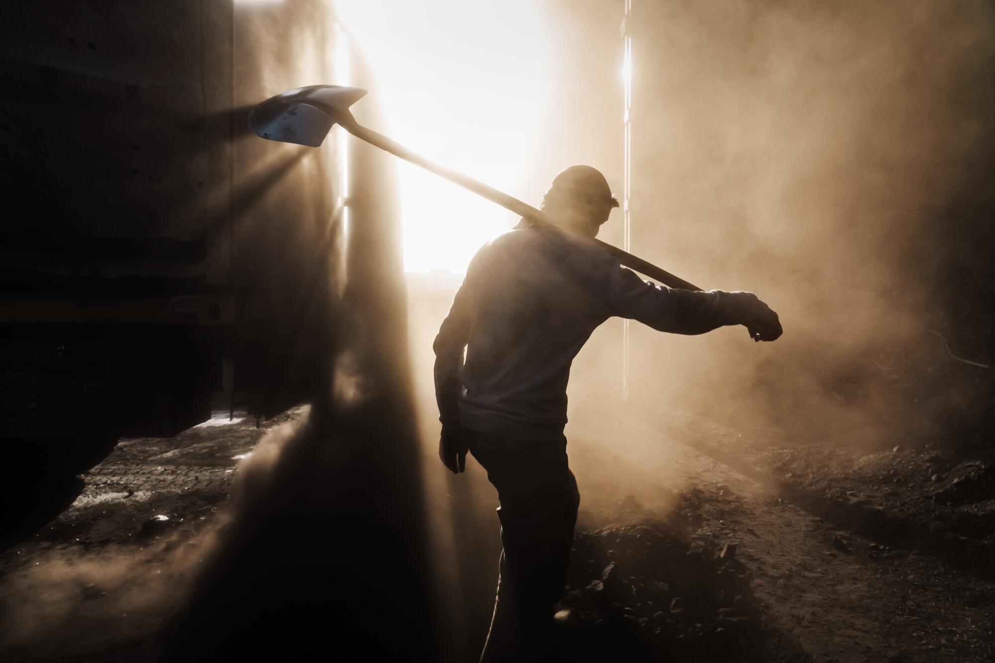 Man with shovel silhouetted in cloud of dust