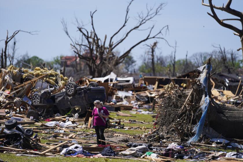 FILE - A woman walks near an uprooted tree, a flipped vehicle and debris from homes damaged by a tornado, March 27, 2023, in Rolling Fork, Miss. While the dangers of tornadoes to mobile homes have long been known, and there are ways to mitigate the risk, the percentage of total tornado deaths that happen in mobile homes has been increasing. (AP Photo/Julio Cortez, File)