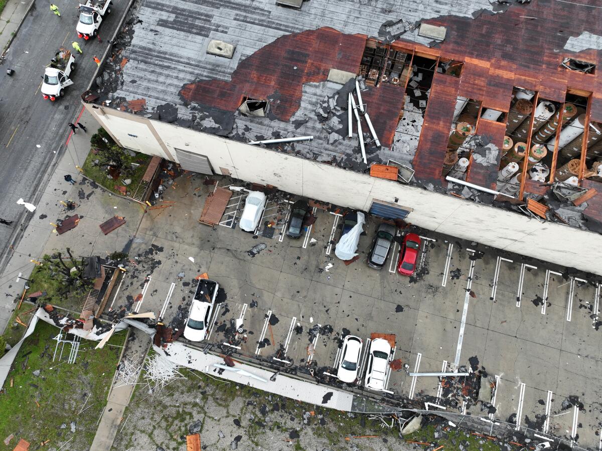 An aerial view of the damaged roof of a commercial building and debris in an adjacent parking lot.