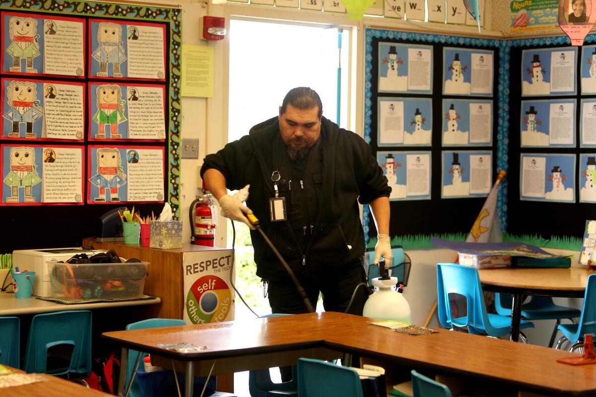 Palm Crest Elementary School custodian Antonio Villavicencio sprays a disinfecting agent onto desks during school deep cleaning while students are away.