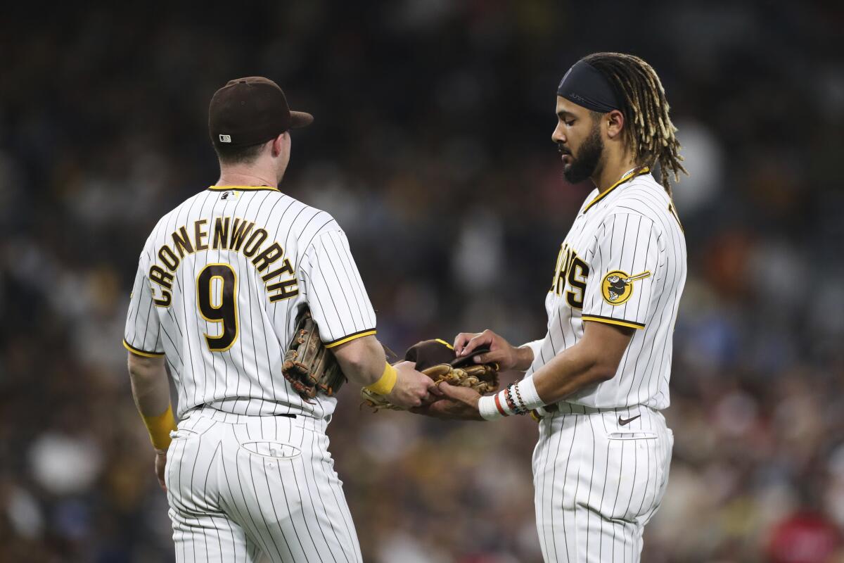 Padres second baseman Jake Cronenworth hands Fernando Tatis Jr. his glove and hat during a game July 29.