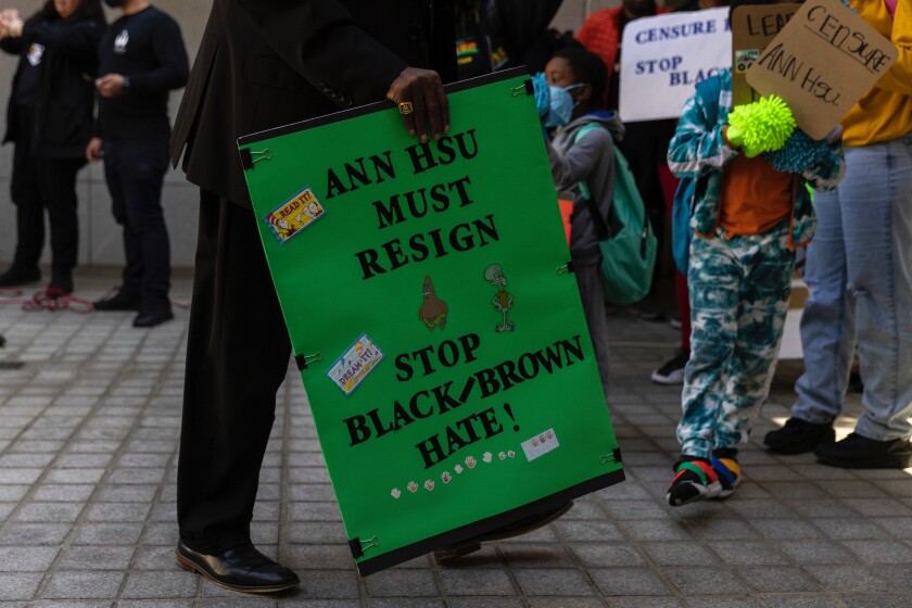 A green sign says Ann Hsu must resign. Stop black/brown hatred