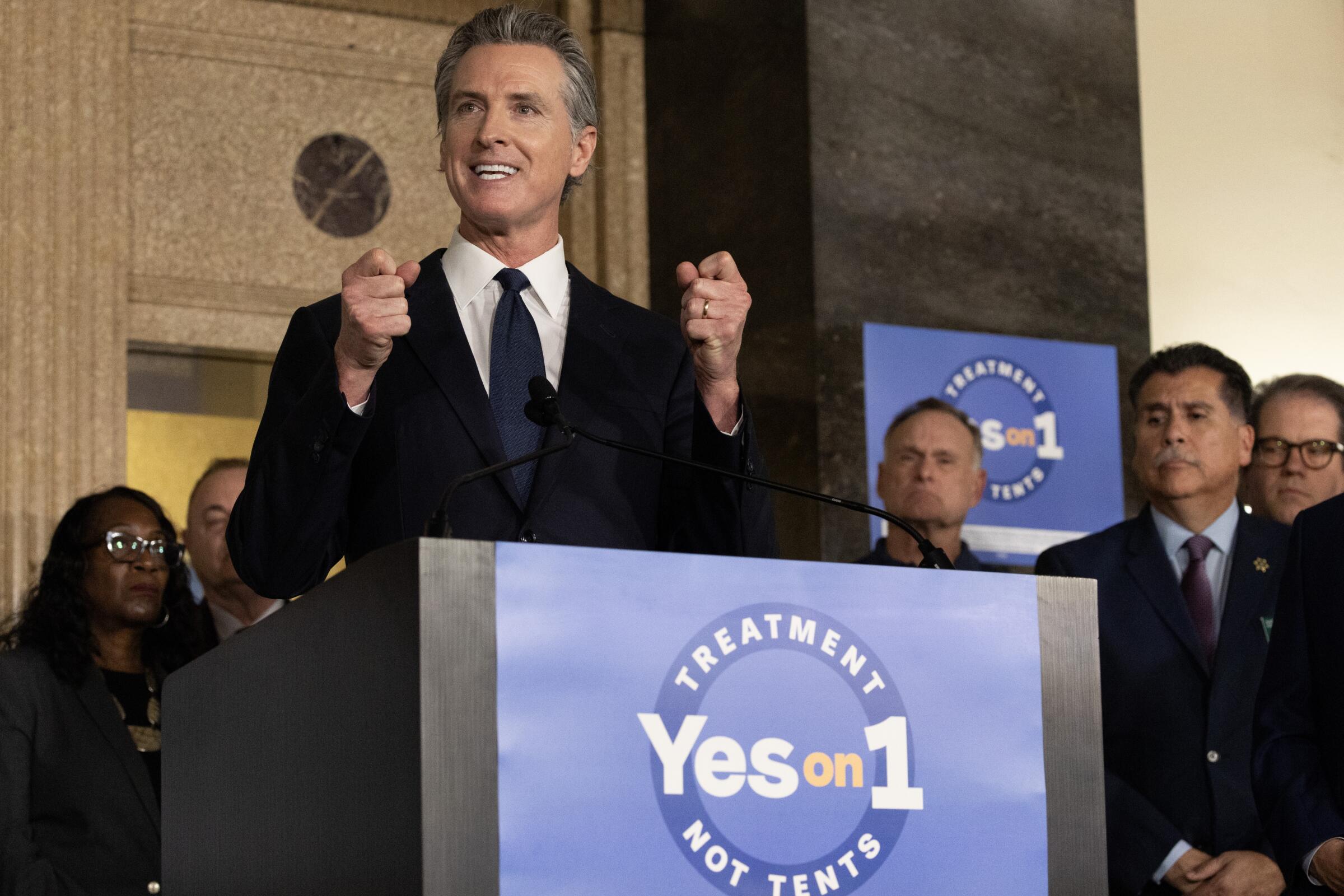 Gov. Gavin Newsom standing in front of a podium that has a blue sign that reads "Yes on 1"