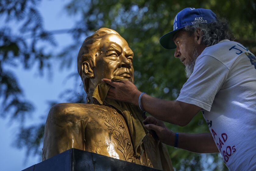 MAYWOOD, CA-JULY 16, 2022: Alex Vanegas, 65, a migrant from Nicaragua, cleans a bust of Nicaraguan poet Ruben Dario, at Maywood Riverfront Park in Maywood. He has been working to clean and renovate the bust since it's been getting deteriorated with rust over the last decade. The Nicaraguan American Opportunity Foundation is an organization that offers support and refuge to migrants from Nicaragua, and also works as a cultural space for those Nicaraguans living in Los Angeles. Vanegas, who is one of those migrants, is part of the organization. He fled the country after being arrested multiple times, spending months in prison and house arrest, and is learning to assimilate to Los Angeles. (Mel Melcon / Los Angeles Times)