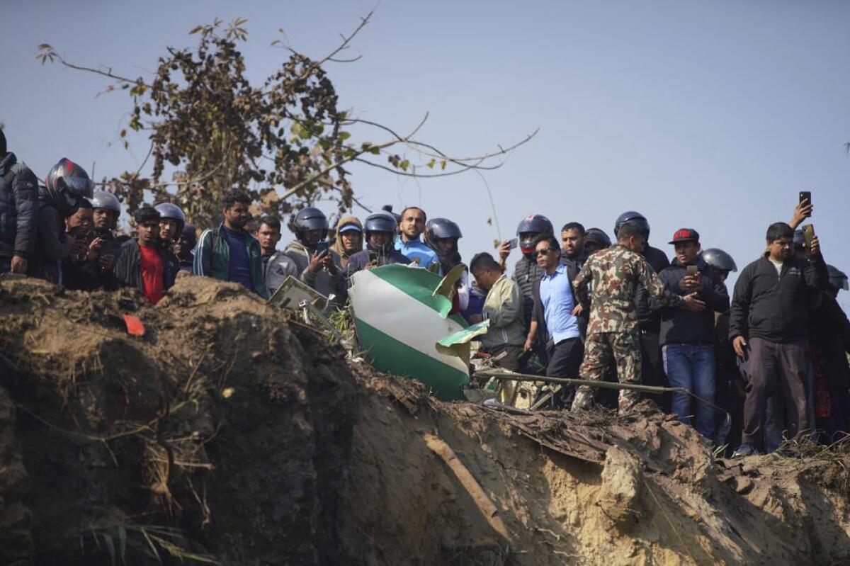 People gather to look at the remains of a plane on dirt terrain