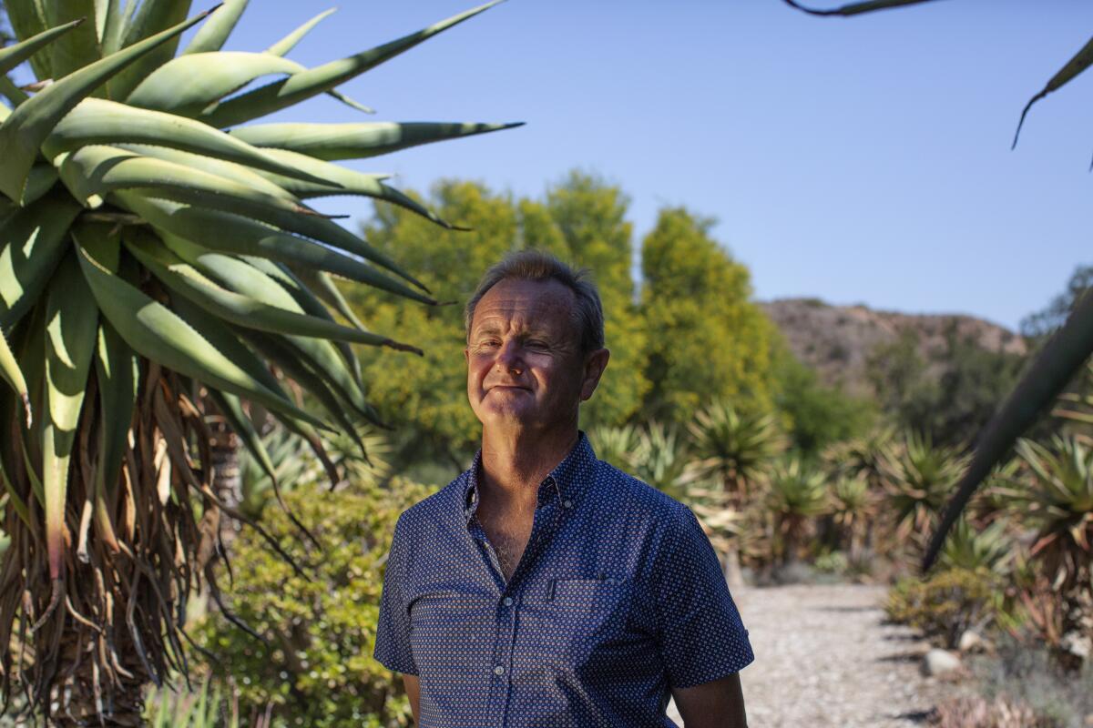 A smiling man stands in a garden.