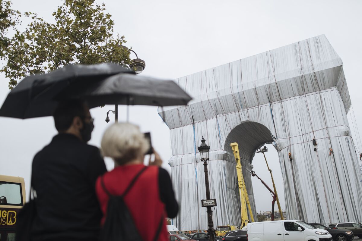 People looking at Paris' Arc de Triomphe swathed in fabric