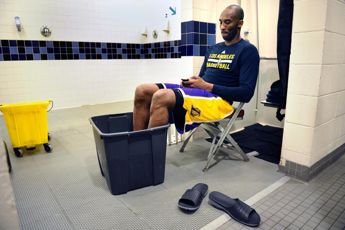 Kobe Bryant checks his phone as he soaks his feet in a bucket of ice water before a game with the Rockets in Houston.
