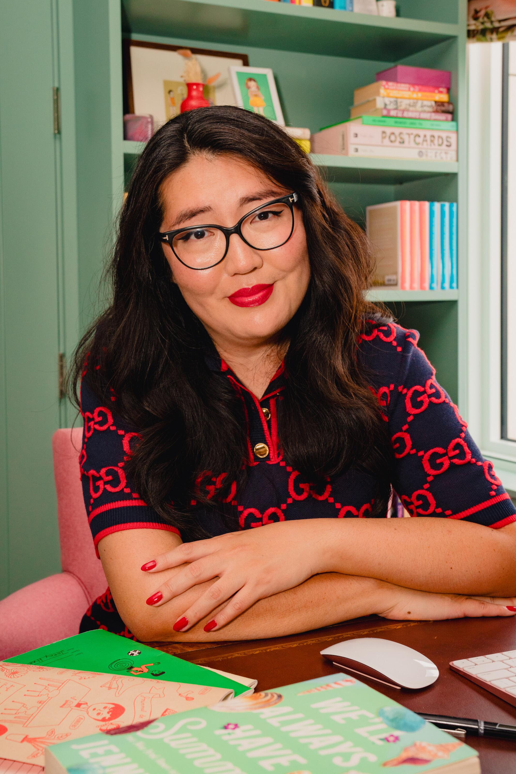 Jenny Han sits with her arms folded on a desk. 