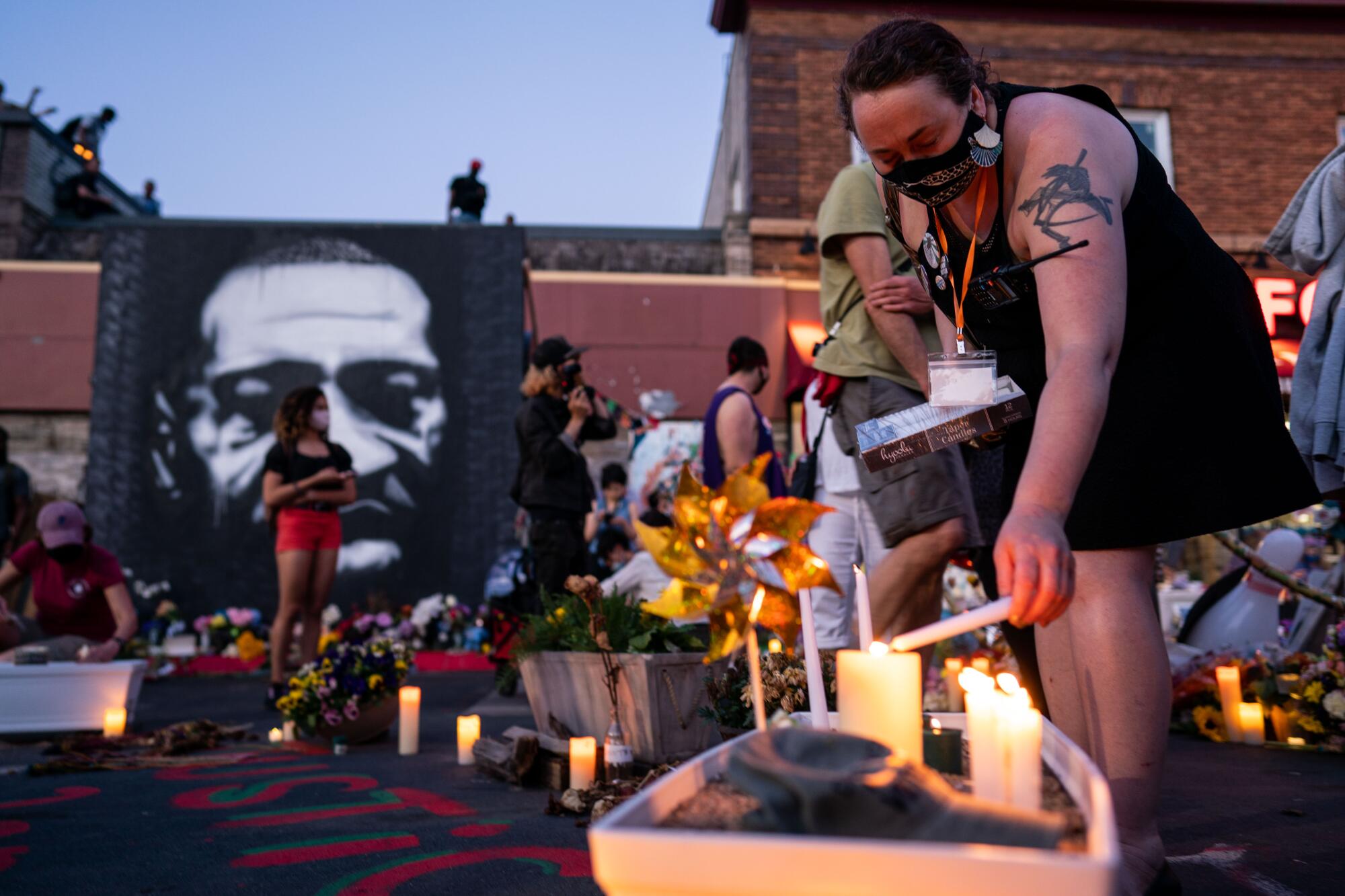 A woman lights a candle from the flame of another at a memorial