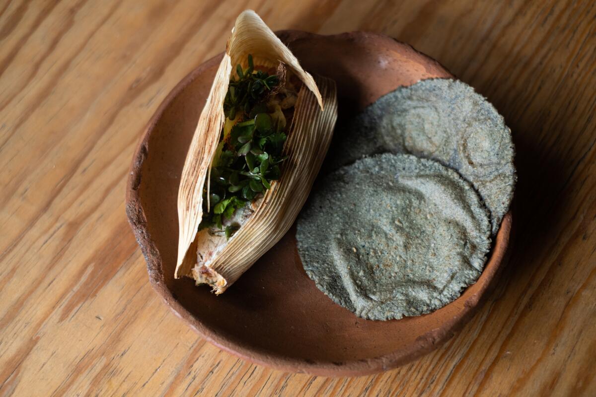 A tamal and blue corn tortillas on a brown plate.