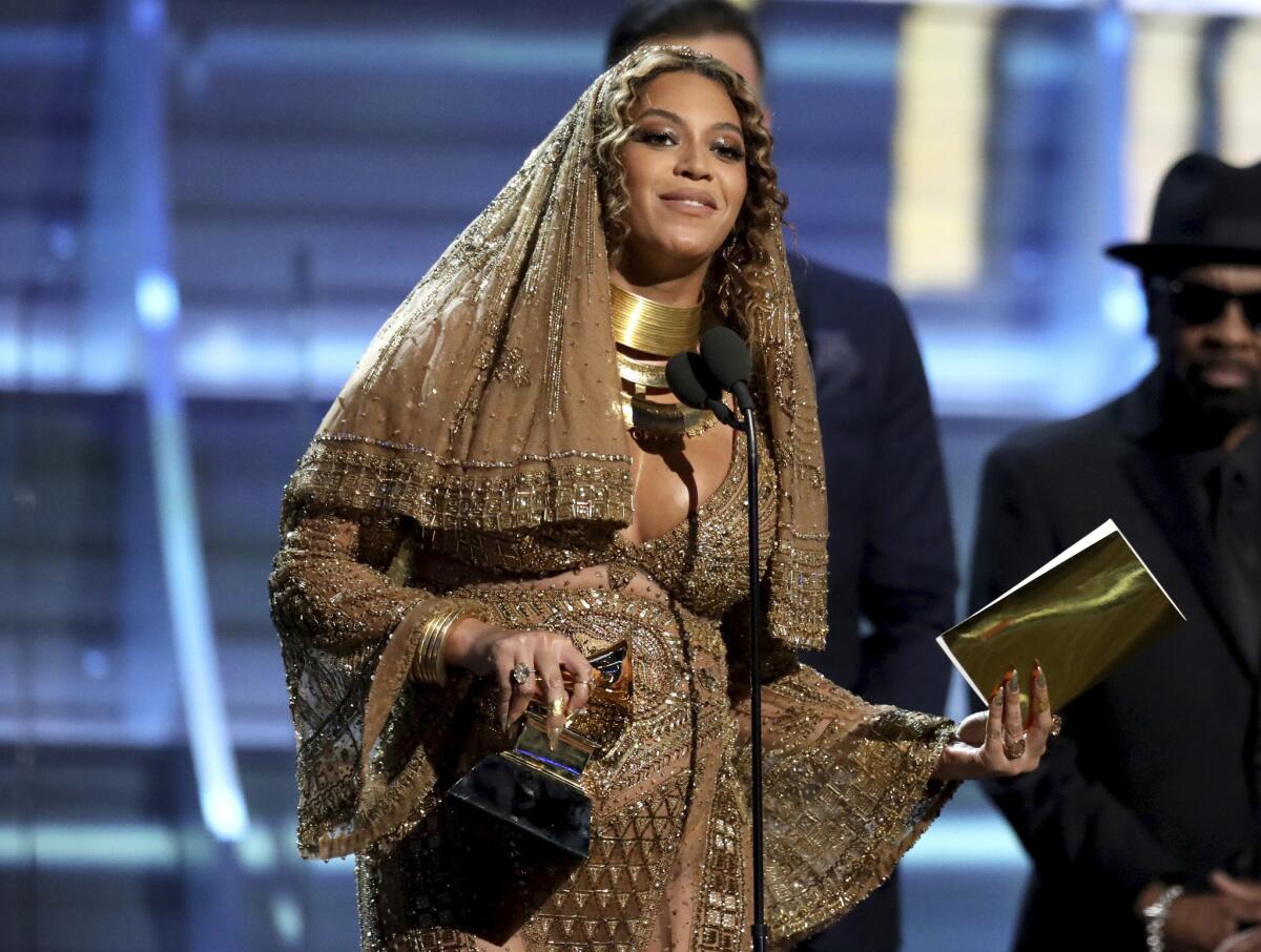 A woman in a jeweled veil speaks onstage