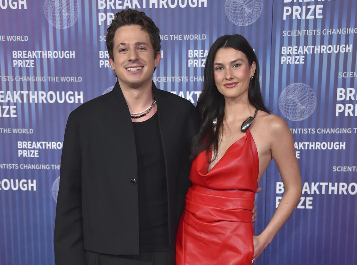 Charlie Puth standing in a black jacket over a black shirt with Brooke Sanson, who wears a strappy red dress 