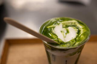 A green-colored drink with a white-colored cream in a glass