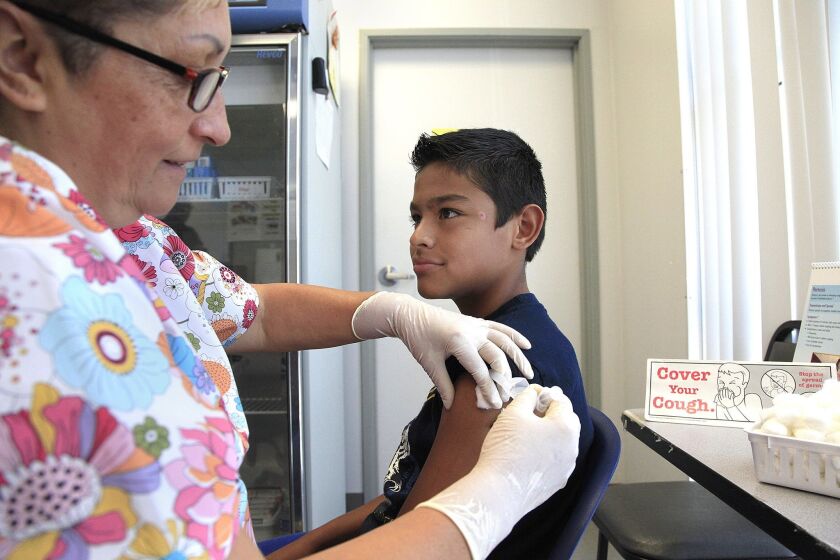 Registered nurse Lupita Baeza, left gives a pertussis vaccine to Julian OLague.