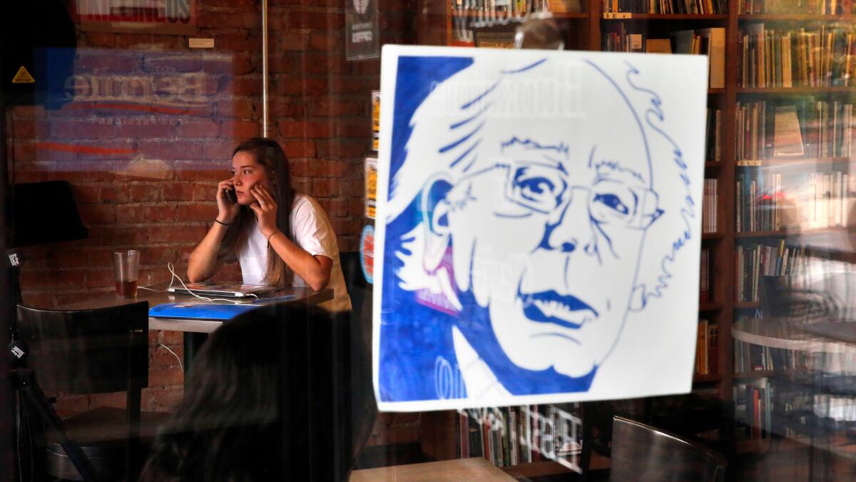 A young woman sits near a number of Bernie Sanders campaign posters that are still posted at the Innisfree Poetry Bookstore & Cafe, a popular hangout for students at the University of Colorado in Boulder.