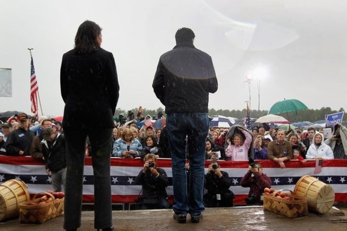 Mitt Romney stands on stage in a rainstorm with South Carolina Gov. Nikki Haley as he speaks during a campaign rally outside a barn at Harmon Tree Farm in Gilbert, S.C.