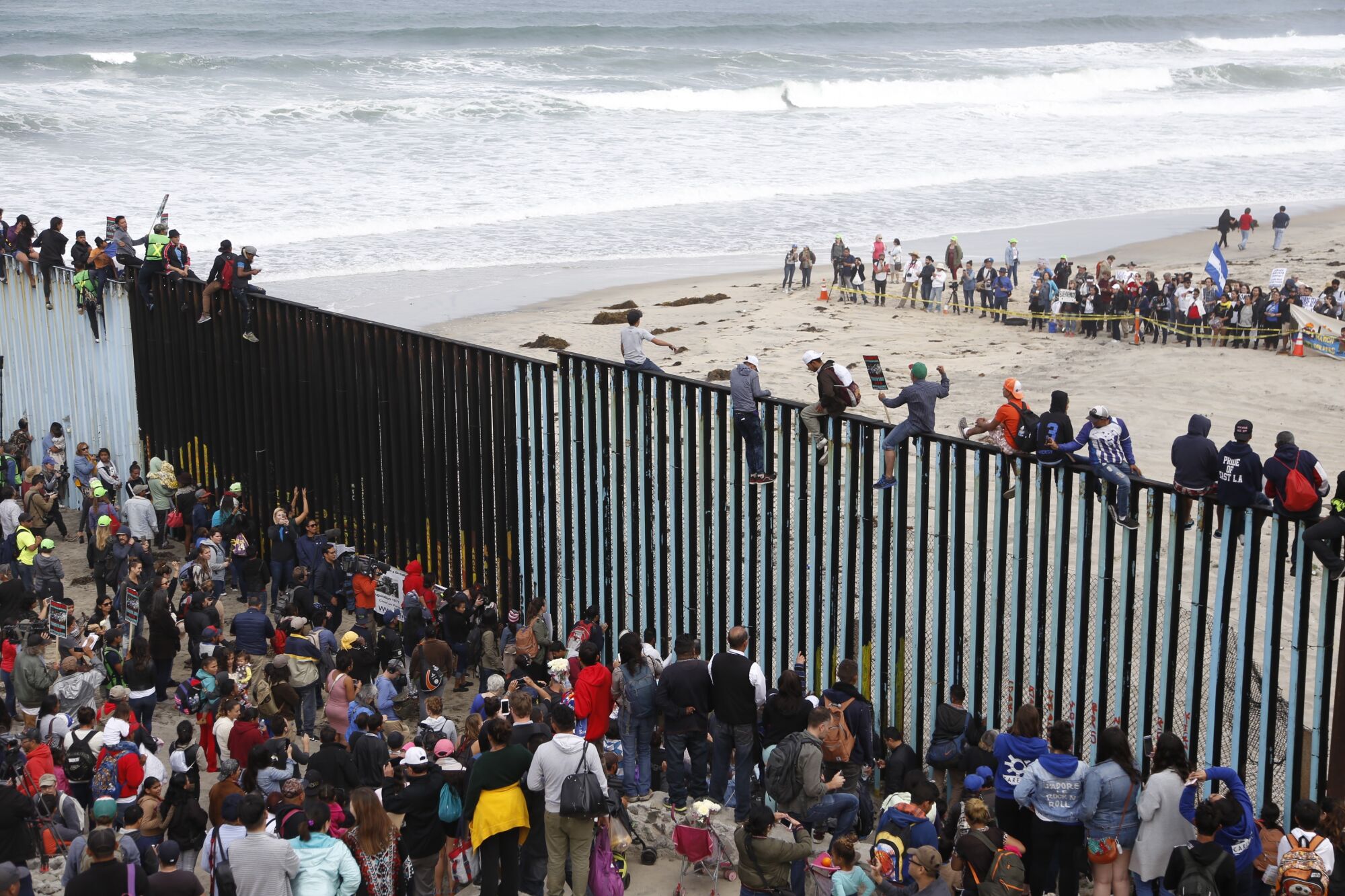 Migrants celebrate their arrival by climbing atop the U.S.-Mexico border fence at Playas