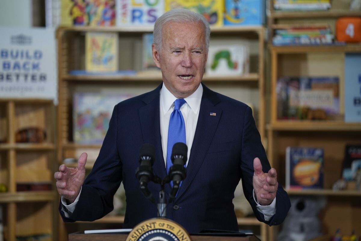 President Joe Biden speaks at a lectern in front of shelves of toys and books