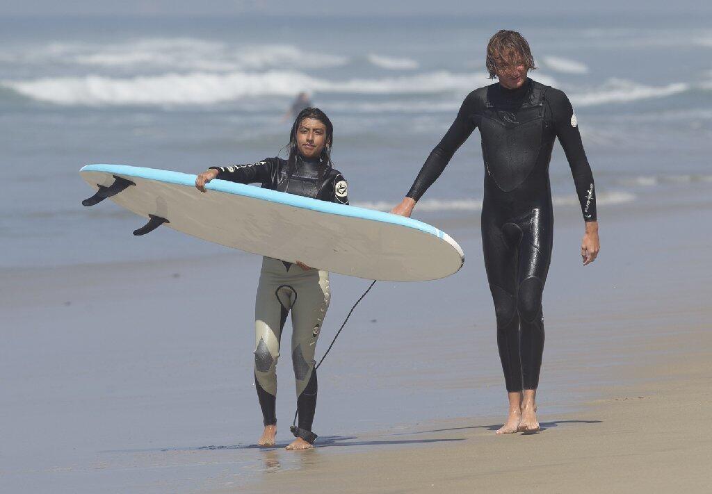 Instructor Josh Giddings, right, walks with surfer Anette Monares after a surf session during Save Our Youth’s Surf Days program in west Newport on Thursday.