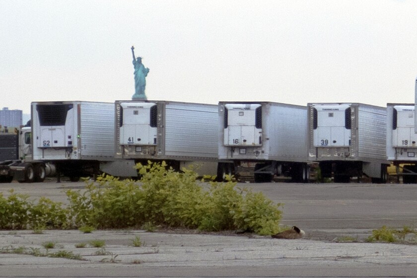 FILE — In this May 6, 2020 file photo, the Statue of Liberty is visible above refrigerator trucks intended for storing corpses that are staged in a lot at the 39th Street pier, in the Brooklyn borough of New York. New York City is still using refrigerated trucks to store bodies of coronavirus victims, more than a year after they were first set up as temporary morgues as deaths surged at at the height of the pandemic. (AP Photo/Ted Shaffrey, File)