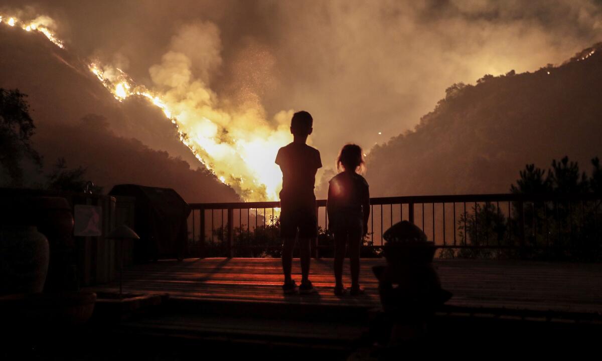 Two children look out at a wildfire in the distance