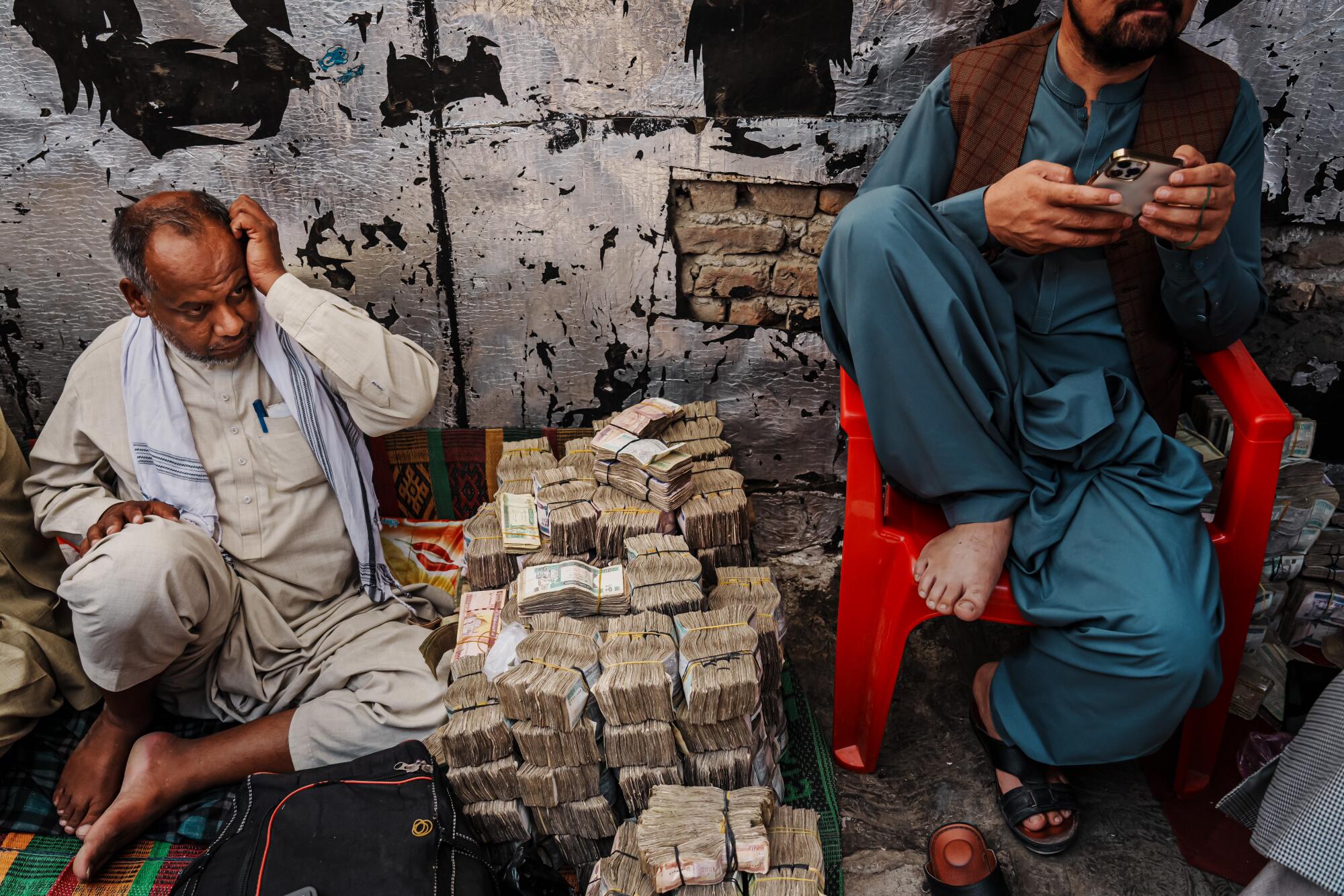 Money-changers next to stacks of Afghan currency