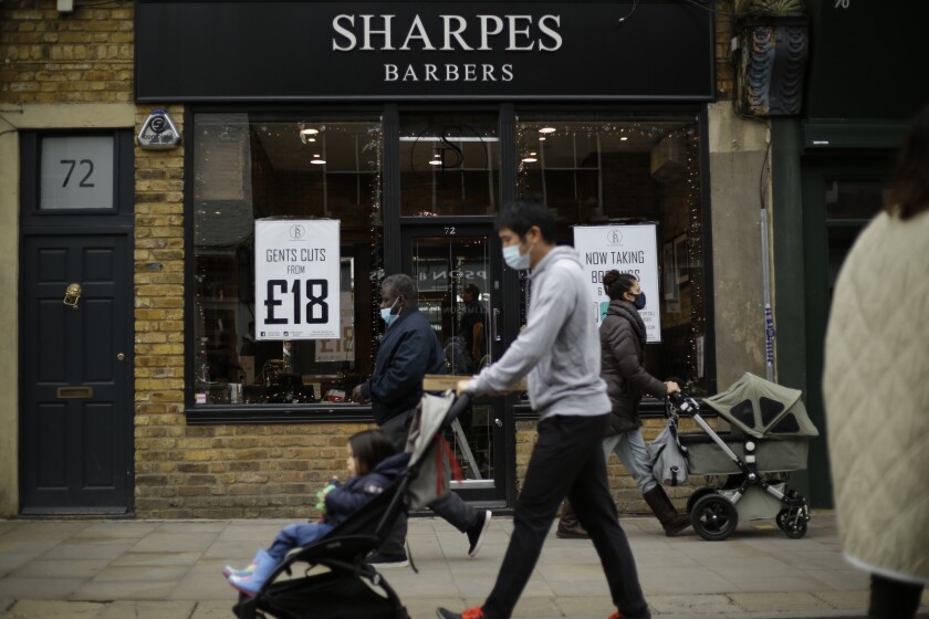 People wearing face masks walk past Sharpes Barbers in east London