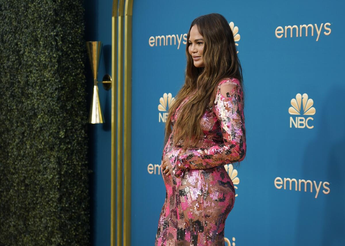 A visibly pregnant woman in a sparkly evening gown poses