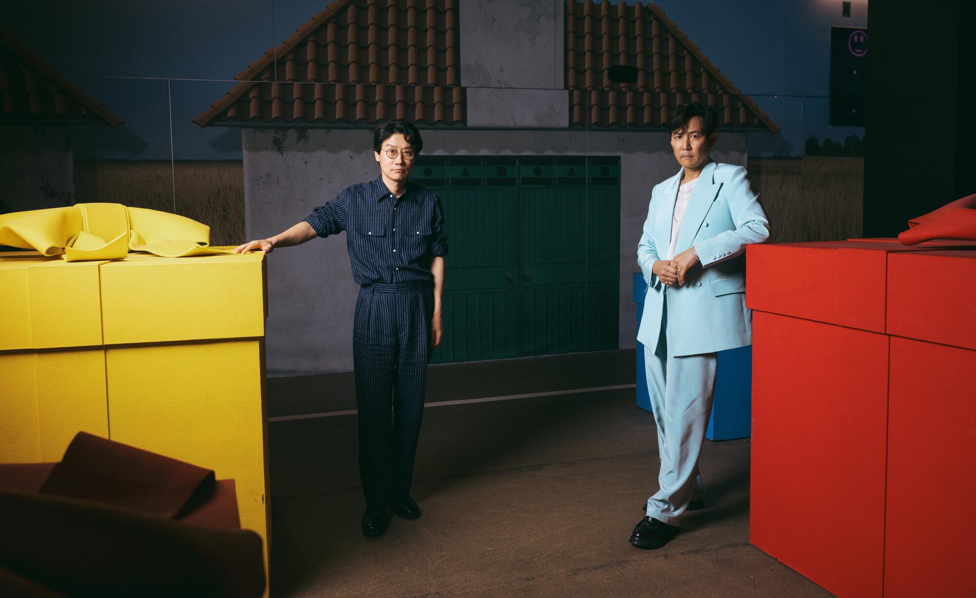 Two men lean against large yellow and gift boxes.