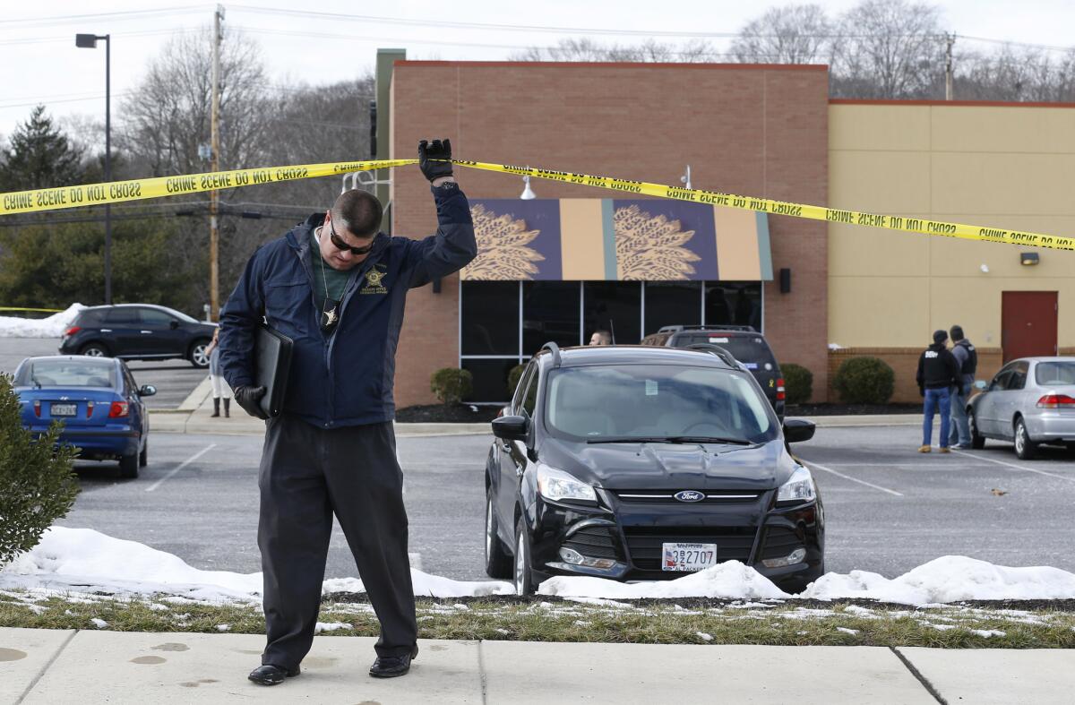 An investigator walks beneath a police tape line at the scene of a shooting at a shopping center in Abingdon, Md.