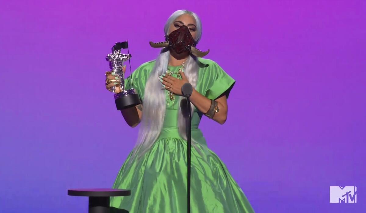 Lady Gaga in a green dress and wearing a face mask, holds an MTV award statue