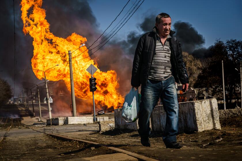 KHARKIV, UKRAINE -- MARCH 25, 2022: A man hurries to walk away from a building that was just hit by Russian bombardment, and caught on fire, in the Moskovskyi district in Kharkiv, Ukraine, Friday, March 25, 2022. (MARCUS YAM / LOS ANGELES TIMES)